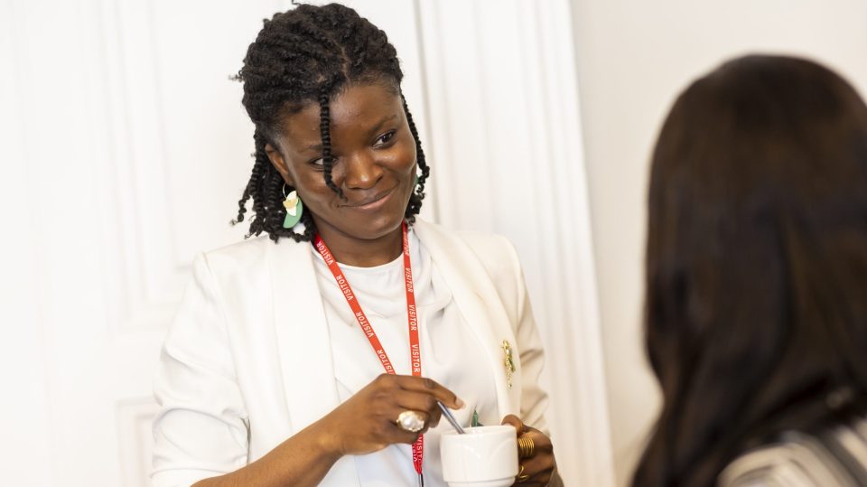 Woman smiling at another woman holding a stirring a mug of tea.