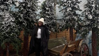 Woman standing in front of Christmas pine trees with a sprinkling of snow on them.